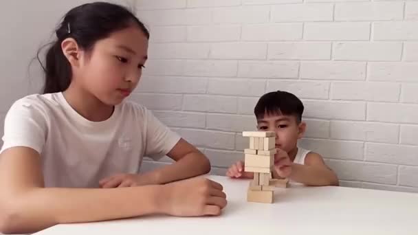 Dzieci bawią się w drewniane puzzle. Jenga upada. Mała dziewczynka i chłopiec wyciągają z wieży drewniane klocki. Życie rodzinne — Wideo stockowe