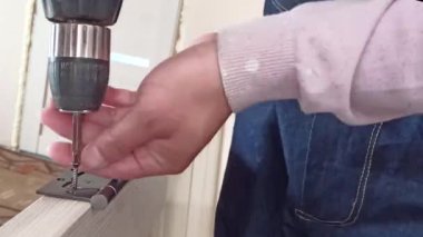 Genç bir işçi iç kapıyı monte ediyor. Adam iç kapıya kilit takmış. ev yapımı düşük hızlı otomatik tornavida. Mobilyalar evde toplanıyor. Elektrikli matkap tahtaya vida takar.