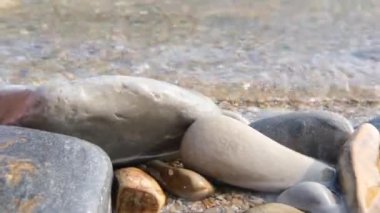 Deniz dalgası taşları yavaşça deniz taşlarının ve dalgaların arka planına doğru sürükledi. Tatil, spa, yaz tatili