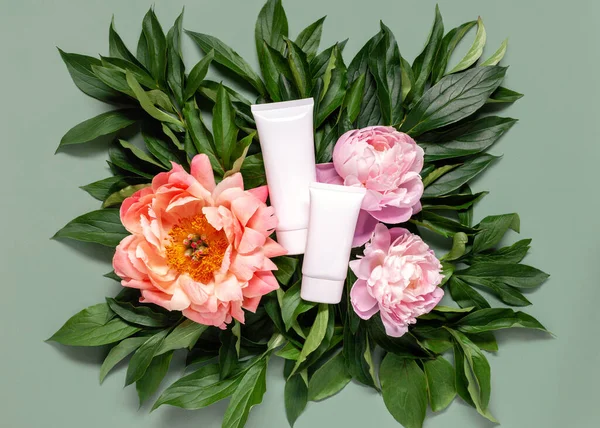 Flat lay composition with cosmetic products and peony flowers on a green background. Top view