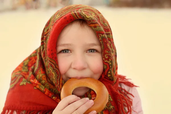 Başörtülü bir kız kışın oturur ve simit yer.