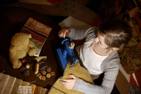 Bir kız dikiş makinesine oyuncak ayı dikiyor.