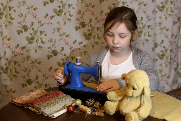 Bir kız dikiş makinesine oyuncak ayı dikiyor.