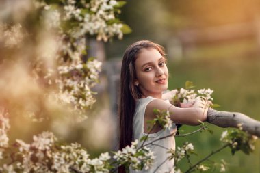 Genç bir kız çiçek açan bir bahçede yürüyor.