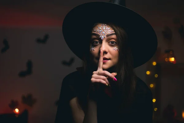 黒の帽子の魔女の衣装の女の子は彼女の鼻の近くに彼女の手を保持し 沈黙を求めて ハロウィーンの雰囲気 — ストック写真