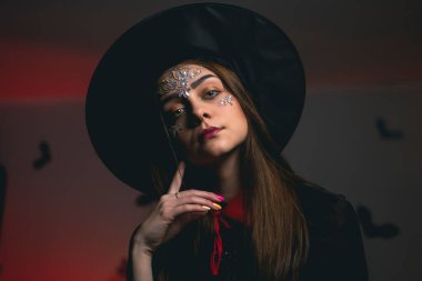 Cadı şapkası ve karnaval kostümü giymiş güzel esmer, yeşil gözleriyle kameraya bakıyor, Cadılar Bayramı partisinde.