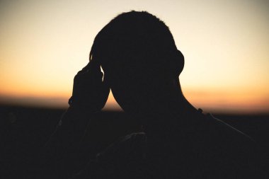 Gün batımında bir adamın silueti. El saçı düzleştirir.
