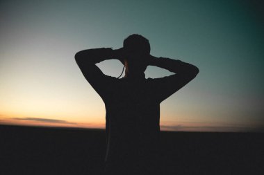 Gün batımında bir adamın silueti. Ellerini başının arkasına koy.