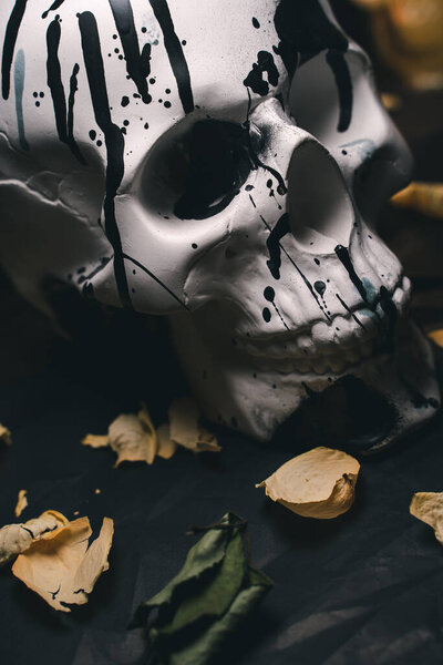 Decorative white human skull in a mysterious setting with burning candles and dry flower petals, black background, close-up, vertical orientation