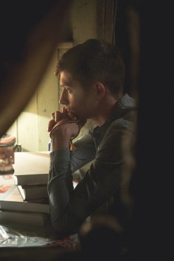 Gömlekli bir adam evde düşünceli bir şekilde oturur. Pencereden çekilen fotoğraf. Bir yığın kitap. Yüksek kalite fotoğraf