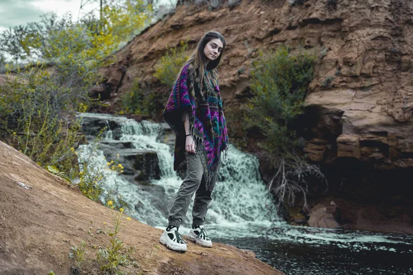 池町の背の高い美少女が滝の背景に立って反対側の人々を見て 彼女と一緒に自然の美しさを楽しむことを求めている — ストック写真