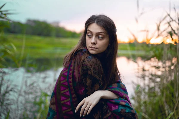 A girl in an Indian poncho looks to the side among the reeds and the lake. sunlight