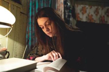 Kız kitabı faiziyle okuyor ve sayfayı çeviriyor. Eski masa lambası.