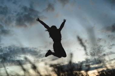 Gün batımına karşı atlayan bir kızın silueti dağlarda özgürlük, doğa ile sevgi ve yeniden birleşme.