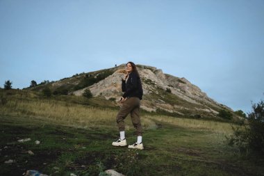Spor kızı turist yüksek bozkırlara tırmanıyor, arkasını dönüyor ve gülümsüyor, uçsuz bucaksızlığa hayran, doğayla yeniden birleşiyor.