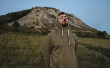 Yeşil kazaklı genç bir adam sırtı dağa dönük duruyor ve bozkırların genişliğine bakıyor, çıplak gökyüzü, yatay yönelim.