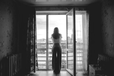 Bir kadın balkonda duruyor ve umutsuzluk, yoksulluk, üzüntü içinde iç çekiyor.