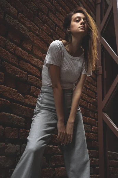 Kırmızı tuğla duvar arkasında poz veren genç bir kadın model. — Stok fotoğraf