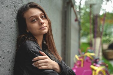 Sırtı gri bir duvara dönük genç bir kadın çok renkli bisikletlerin yanında duruyor, çok renkli arka plan.