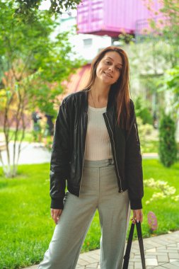 Genç bir kadın yeşil bir parkta yürüyor, gülümseyen bir kız, parlak renkler.