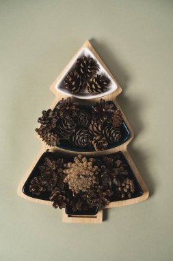 Çam kozalaklarıyla dolu bir ağaç şeklinde Noel vazosu açık yeşil bir arka planda yatıyor.