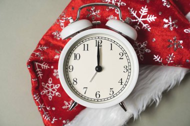 Kırmızı bir Noel şapkasının arkasında beyaz alarmlı saat var. Yeni yılda, saat işçileri gece yarısını gösteriyor.