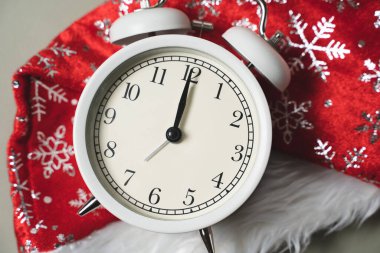 Beyaz alarmlı saat yeni yılın arka planında duruyor. Kırmızı başlık, yeni yıl, gece yarısı.