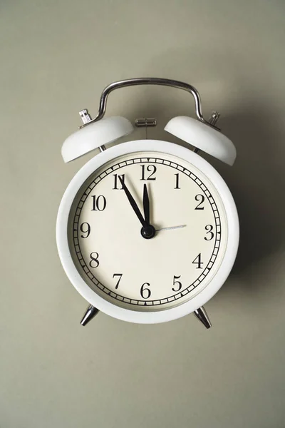 an alarm clock with a dial lies on a gray background, the time brings it closer to a new day, vertical orientation