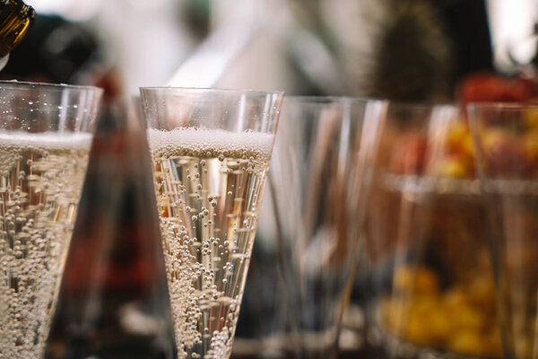Wine glasses are filled with champagne from a glass bottle, buffet table at the opening of a beauty salon, blurred background, large plan