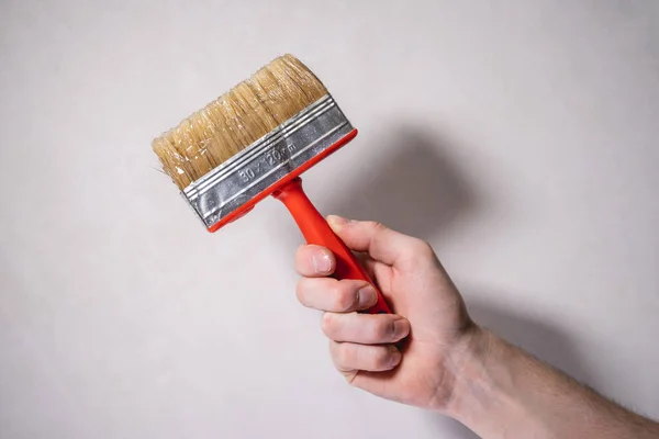 A man\'s hand holds a brush for applying glue to the wall, for further wallpapering, renovating a new house