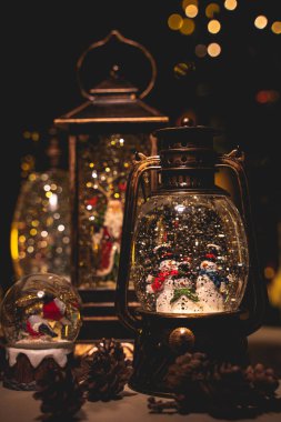 Kar efektli Noel feneri ve içinde biblolar olan çam kozalakları