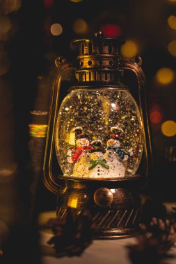 Kar yağışı efektli ve içinde kardan adam figürleri olan Noel feneri