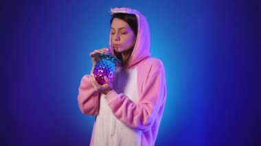Pembe pijamalı hoş bir kadın elinde ananas şeklinde neon bir bardak tutuyor.