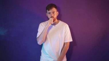 Beyaz tişörtlü sakallı bir adam elinde elektronik bir sigara tutuyor.