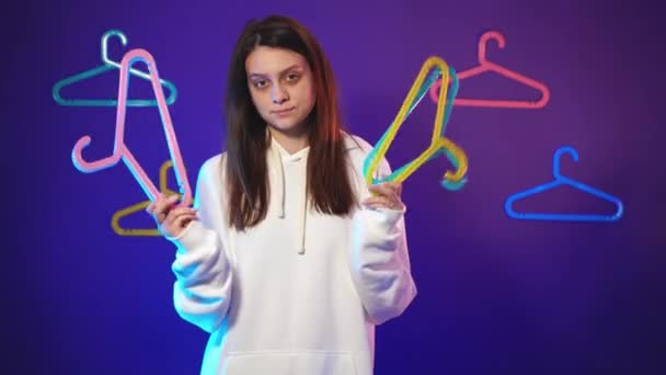 Vrouw in een witte hoodie met kleurrijke heldere hangers in haar handen — Stockvideo