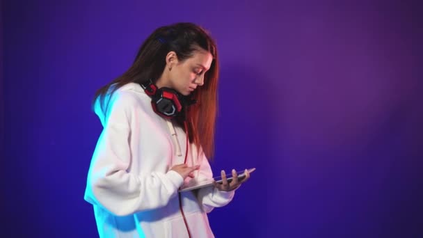 Piękna brunetka ze słuchawkami na szyi trzyma tablet w rękach — Wideo stockowe