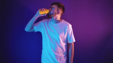 Sakallı bir adam mor arka plandaki demir bir kutudan su içer.