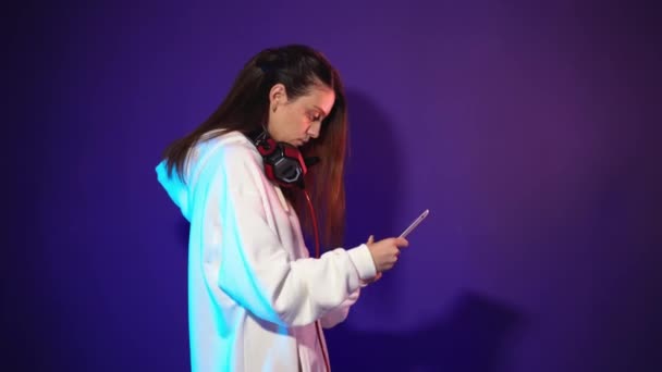Beautiful brunette gamer with headphones on his neck holds a tablet in his hands — Stock Video