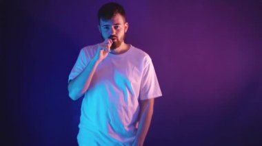 Beyaz tişörtlü genç sakallı adam elinde elektronik bir sigara tutuyor.