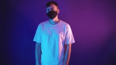 Beyaz tişörtlü sakallı bir adam yüzünden koruyucu bir maske çıkarıyor.