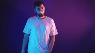 Beyaz tişörtlü genç sakallı adam elinde elektronik bir sigara tutuyor.