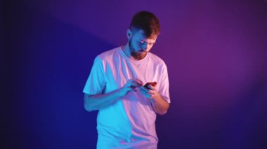 Beyaz tişörtlü genç sakallı adam elinde bir akıllı telefon tutuyor.