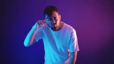 Beyaz tişörtlü genç bir adam elinde bir büyüteç tutuyor.