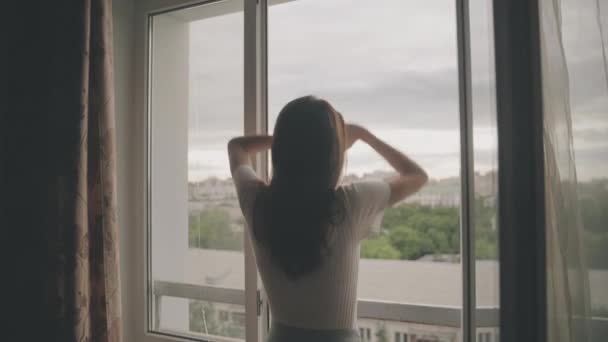 Beautiful brunette stretches slowly and looks out the window — Stock Video