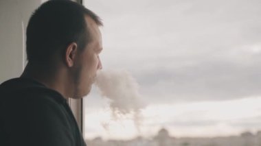 Evin balkonundaki genç adam pencereden içeri doğru bakıyor.