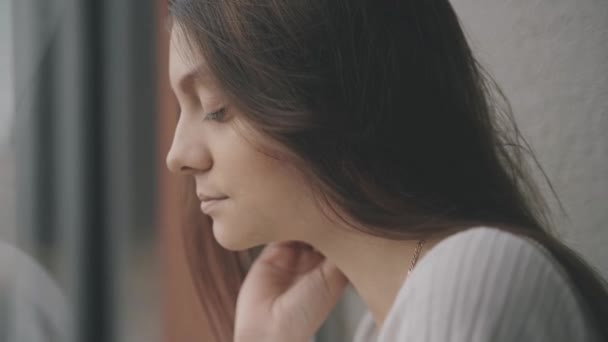 A young woman stands near the window and looks thoughtfully at the city — Stock Video