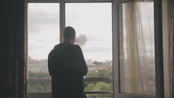 Νεαρός άνδρας στο μπαλκόνι του σπιτιού κοιτάζει στην απόσταση από το παράθυρο — Αρχείο Βίντεο