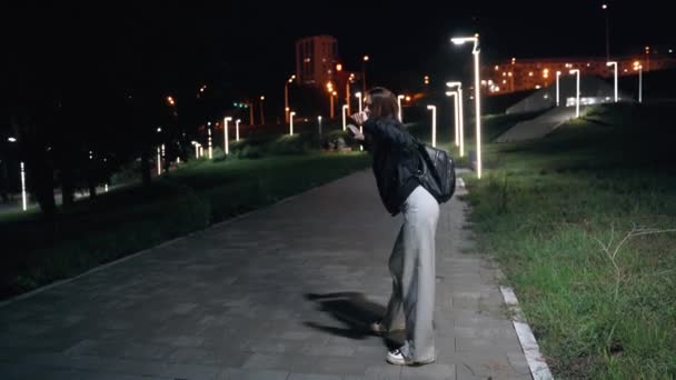 Jovem mulher ambiciosa em calças queimadas está alegremente dançando em um parque noturno — Vídeo de Stock