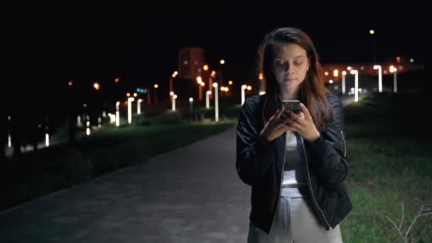 Uma bela mulher sociável fica em um parque noturno com belas lanternas — Vídeo de Stock