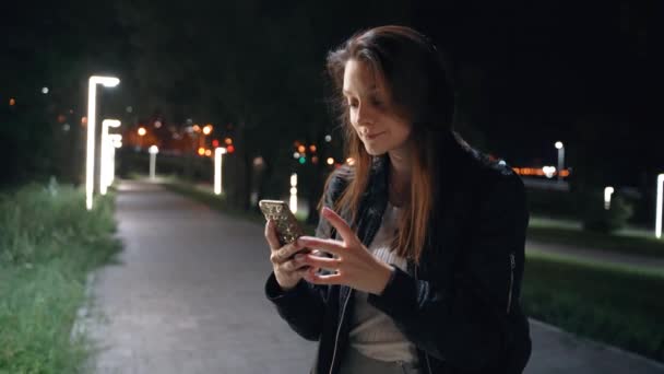 Genç bir kadın gece parkında duruyor, saçını düzleştiriyor. — Stok video
